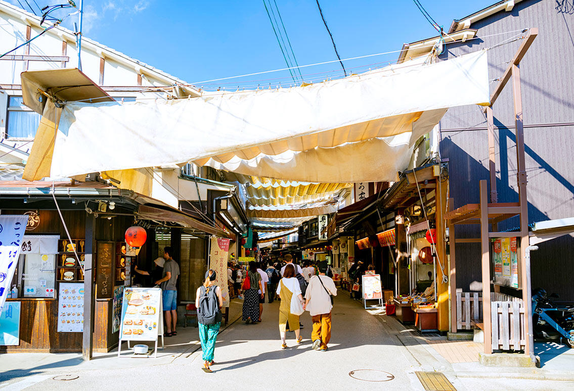 宮島表参道商店街の風景。頭上に大きな白い日よけ布が張られ、観光客が行き交っている。
